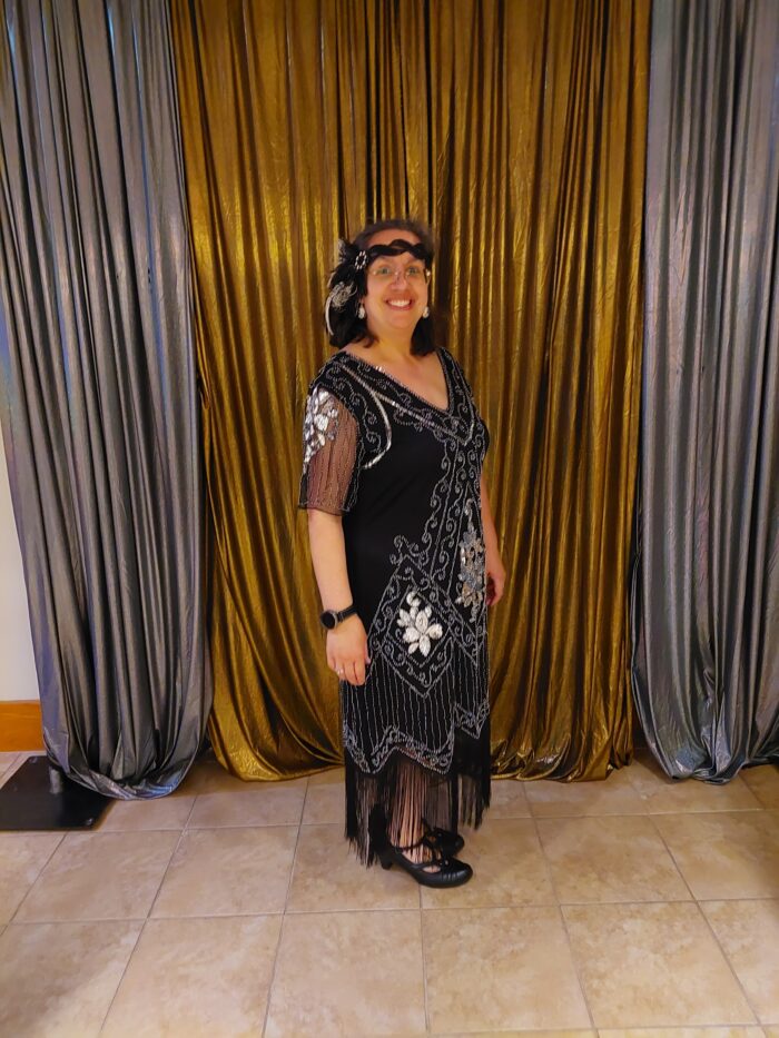 WMA art educator Janin Wise, dressed up for the 1920s themed banquet in a black and silver flapper dress in front of a silver and gold background