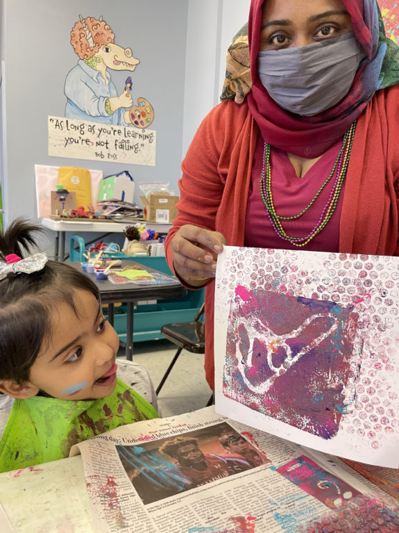 A toddler and her mother create a monoprint in an art classroom.