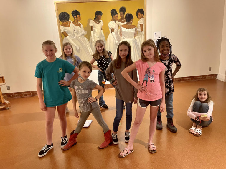 A group of young girls pose with a painting behind them.