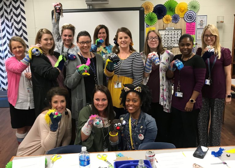 A group of teachers post with their newly created sock puppets.