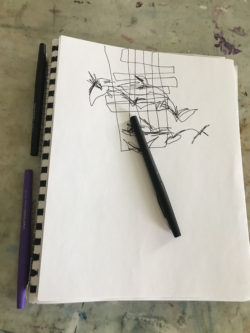 A white notebook is on a table with a sketch of birds on it and a pen laid across it. 